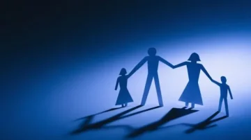Silhouettes de personnages en papier représentant une famille se tenant la main sur un fond bleu. Les ombres créent une ambiance chaleureuse et unie, symbolisant l'amour familial et la connexion.