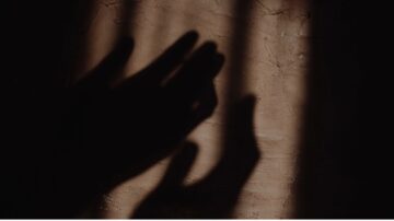 ظلال يدين تتداخل على جدار ملون، تعكس أضواء وظلالًا دافئة، تعبر عن لحظة من التعبير الفني والعمق العاطفي.