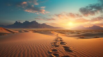صورة لصحراء شاسعة تحت سماء ملونة بألوان الغروب. تظهر آثار أقدام على الرمال الناعمة، مع جبال في الخلفية تتناغم مع الأفق. تعكس الألوان الدافئة جمال الطبيعة وهدوء المنظر.