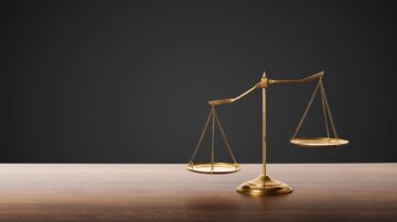ميزان قانوني ذهبي اللون موضوعة على طاولة خشبية، مع خلفية داكنة. يمثل العدالة والمساواة في القانون.