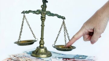 ميزان قانوني قديم مع يد تشير إلى أحد الصواني، موضوع فوق أوراق نقدية يورو ملونة. يرمز للصواب والخطأ في القضايا المالية.