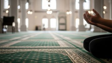 أسباب عدم استجابة الدعاء يتصور بشخص جالس على سجادة صلاة خضراء في مسجد، يرفع يديه للدعاء.