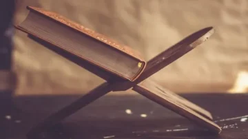 Livre posé sur un support en bois, avec une couverture marron, sur une surface sombre. Arrière-plan flou et texturé.