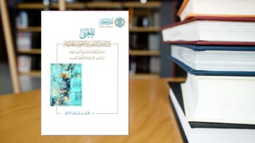 غلاف كتاب بعنوان "المعجم" مع تصميم فني بالألوان الزرقاء على خلفية خشبية. الكتاب موضوع على طاولة بالقرب من مجموعة من الكتب المكدسة، مما يبرز الأجواء الأكاديمية.