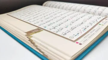 Livre ouvert du Coran, montrant des pages avec du texte en arabe. La reliure est visible sur le côté gauche, et le fond est neutre. Le texte est clair et bien formaté, soulignant l'importance religieuse et culturelle du livre.