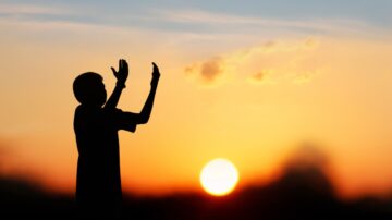 Silhouette of a child with raised hands against a vibrant sunset, embodying the spirit of hope and trust found in belief in the divine decree (Al-Qadar)