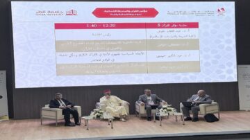 مؤتمر حول التعليم العالي في قطر، يتضمن جلسة حوارية مع ثلاثة متحدثين، حيث يتناولون موضوعات متعددة تتعلق بالتعليم والابتكار. خلفية الشاشة تعرض جدول الجلسات مع توقيتات وأسماء المتحدثين. الأجواء رسمية ومهنية، مع وجود طاولات مزينة بالزهور.