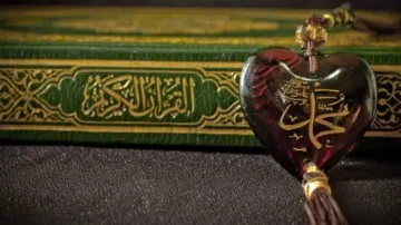 Coran ouvert avec un marque-page en forme de cœur, orné d'inscriptions arabes dorées. Le fond est sombre, mettant en valeur la texture riche de la couverture du livre.