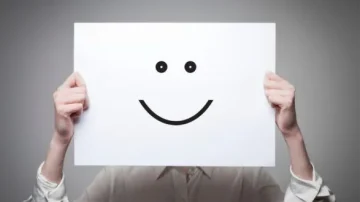 Personne tenant une feuille blanche avec un smiley souriant, fond gris neutre, symbole de bonheur et de positivité.