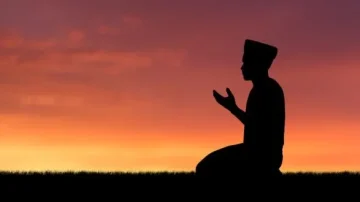Silhouette d'un homme en prière au coucher du soleil, avec des couleurs vives dans le ciel. Moment spirituel symbolisant la foi et la méditation.