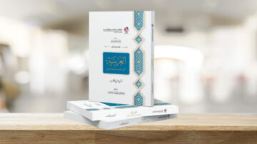 كتاب "العربية: دراسة في أسس اللغة" موضوع على طاولة خشبية، مع تصميم أنيق يغلب عليه اللون الأبيض وزخارف زرقاء، يظهر في خلفية مشوشة تعكس بيئة داخلية.