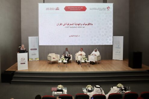 ندوة حول الألوسي ودراسته للقرآن، تتضمن ثلاثة متحدثين يجلسون على منصة، مع وجود لافتة خلفهم تحمل عنوان الندوة. الغرفة مزينة بأثاث حديث وزهور.