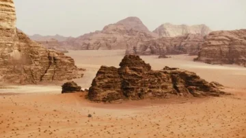 Paysage désertique du Wadi Rum en Jordanie, avec des formations rocheuses majestueuses et un ciel dégagé. Les dunes de sable s'étendent à perte de vue, créant un environnement naturel spectaculaire.