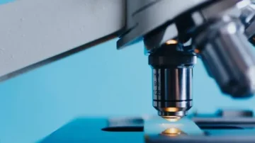Microscope objectif en gros plan, mettant en évidence la lentille et l'éclairage, sur fond bleu. Idéal pour des recherches scientifiques et des études en biologie.