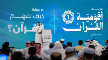 ورشة عمل تتعلق بفهم القرآن، مع متحدث يقف على منصة أمام جمهور. الخلفية تحمل شعار المنتدى وأسلوب تصميم عصري، وتظهر تفاصيل الحدث بوضوح.