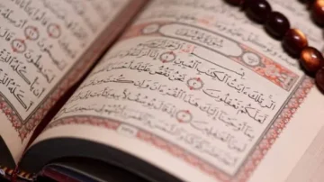 Livre ouvert du Coran avec des pages arabes bien visibles, entouré d'un chapelet en bois. Le texte présente des versets calligraphiés, illustrant la beauté de la littérature islamique.
