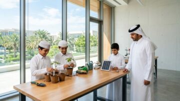 أطفال يرتدون الزي التقليدي الإماراتي يزرعون نباتات في أوعية على طاولة عمل، مع وجود معلم يراقبهم. في الخلفية، حديقة خضراء ونافذة كبيرة تسمح بدخول الضوء الطبيعي، مما يخلق بيئة تعليمية ملهمة.